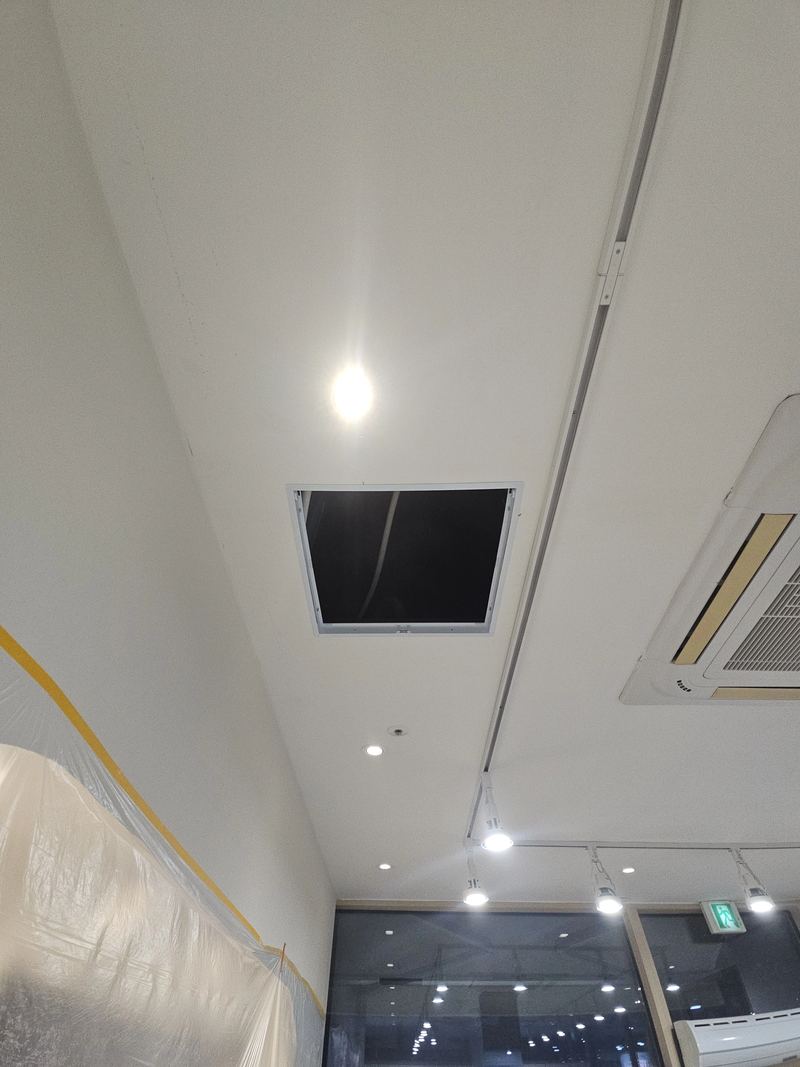 복도 천장에 설치된 검은색 점검구와 주변 조명, 시스템 에어컨이 함께 보이는 모습